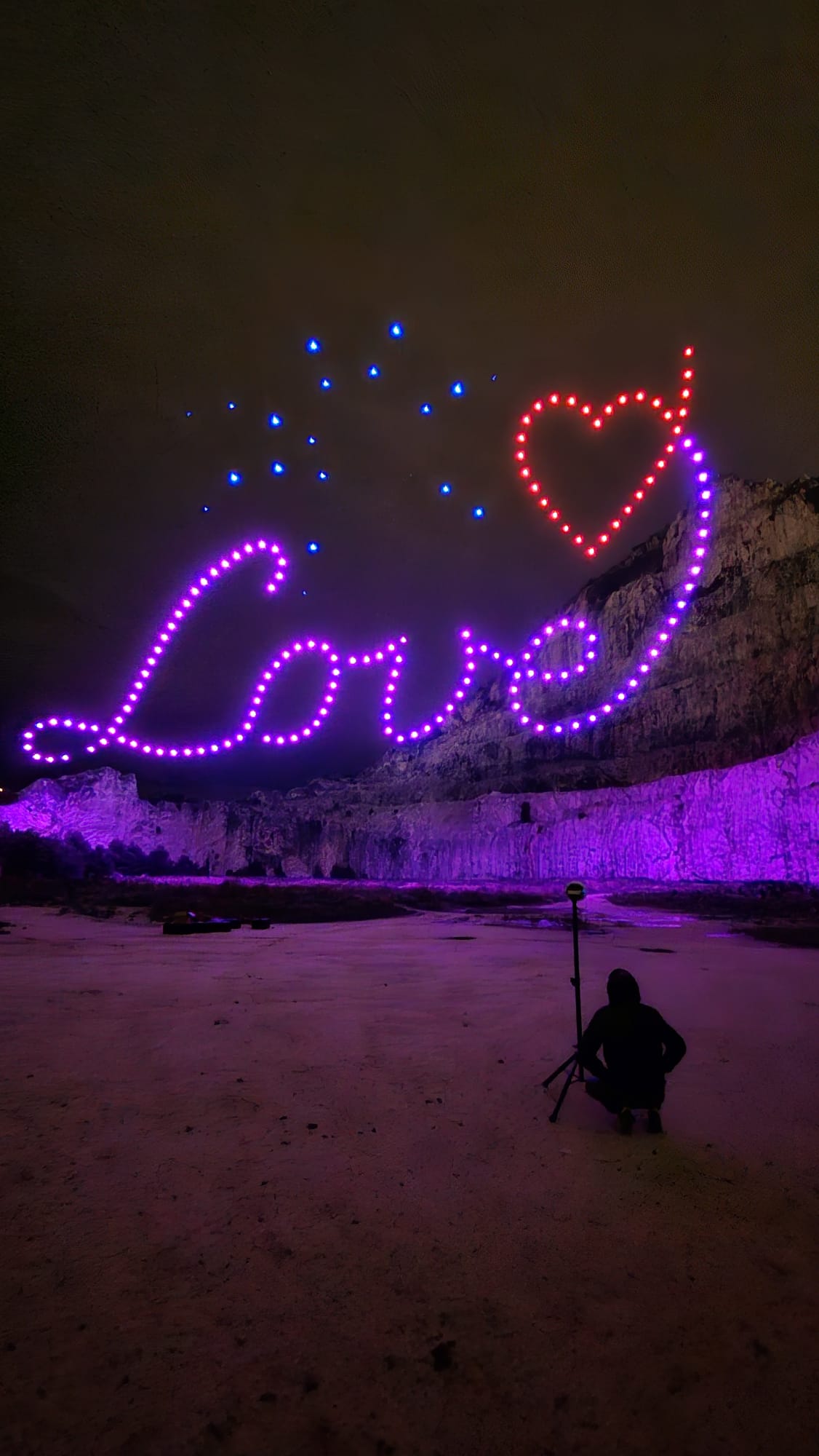 Drones spelling 'Love' with a heart above a cliff at night