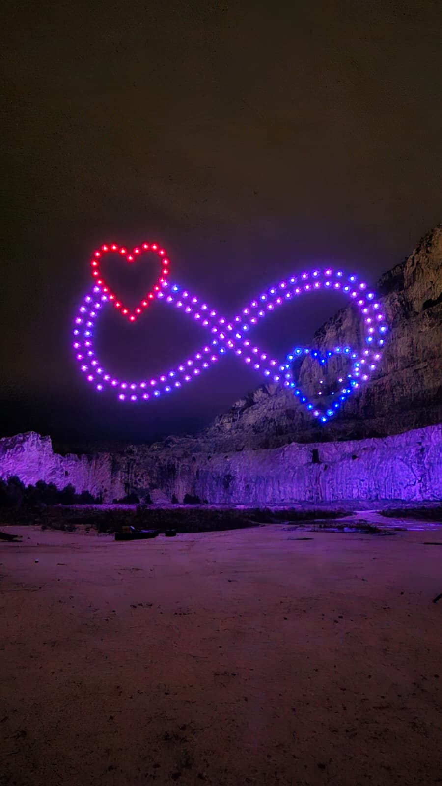 Drone infinity symbol with hearts above a rocky cliff