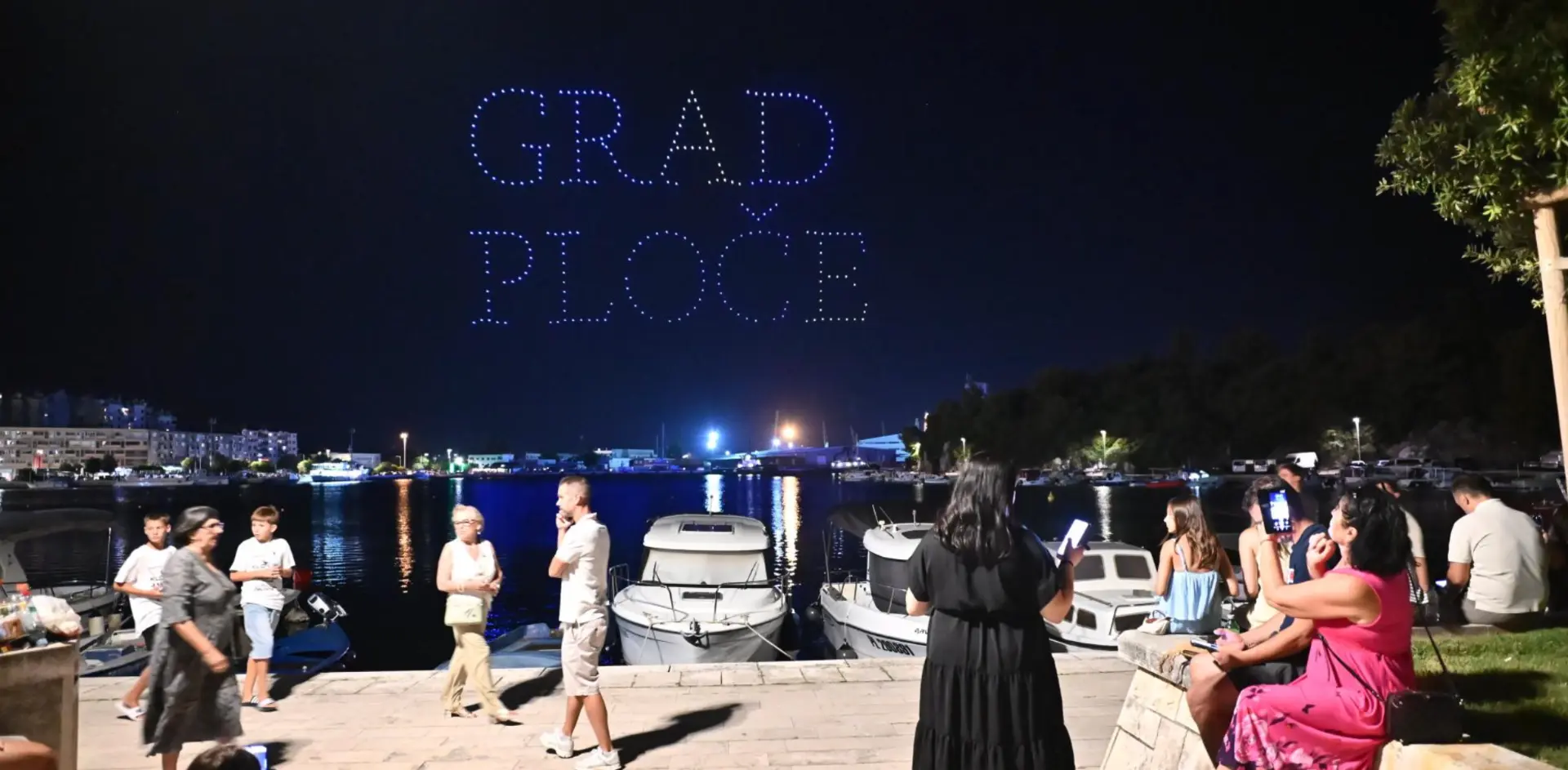 Drones spelling 'GRAD PLOČE' above a harbour crowd at night