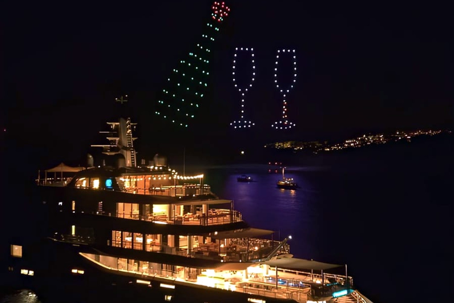 Champagne bottle and flutes formed by drones above a luxury yacht at night