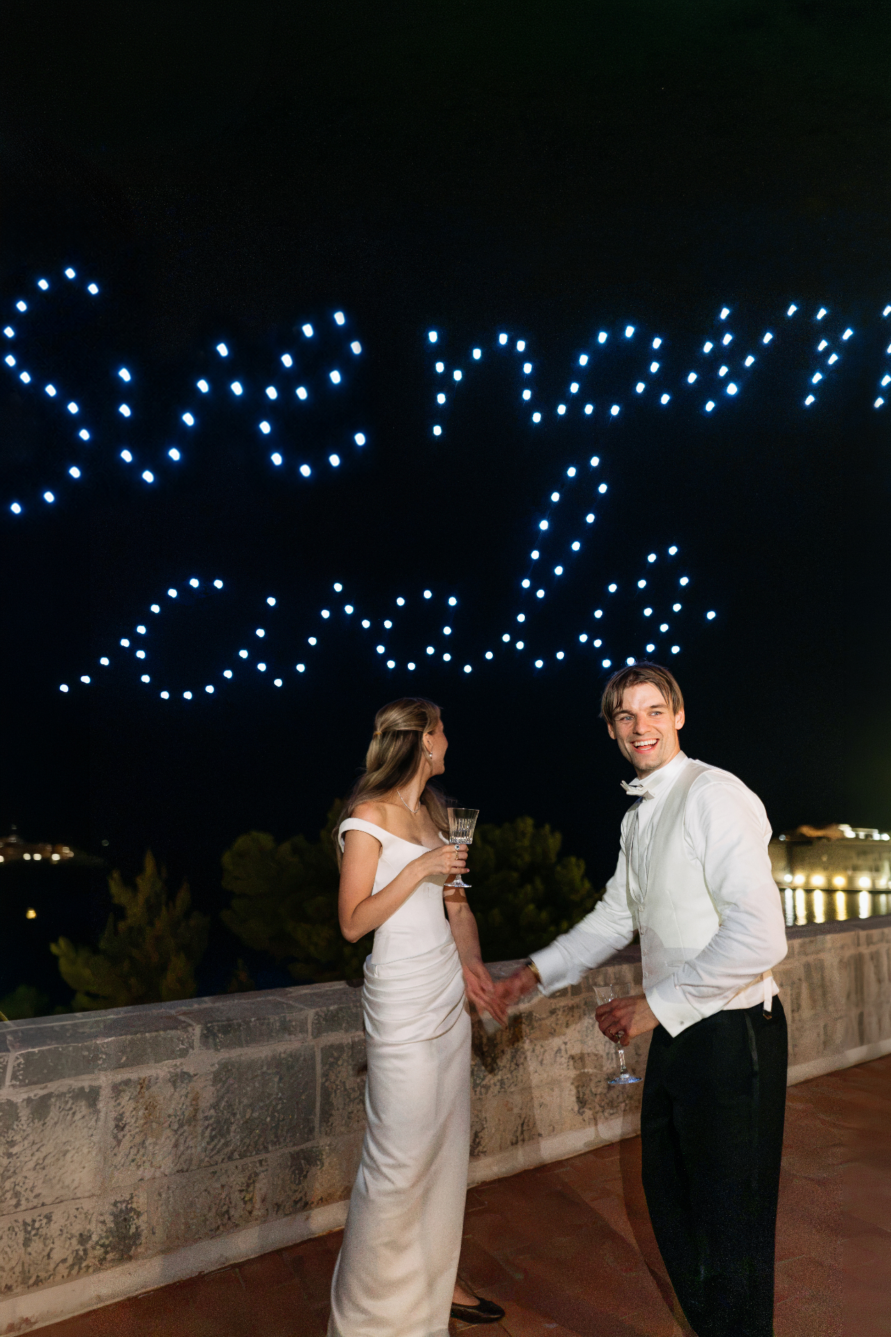 Drones spelling 'She said yes!' above a coastal terrace at night