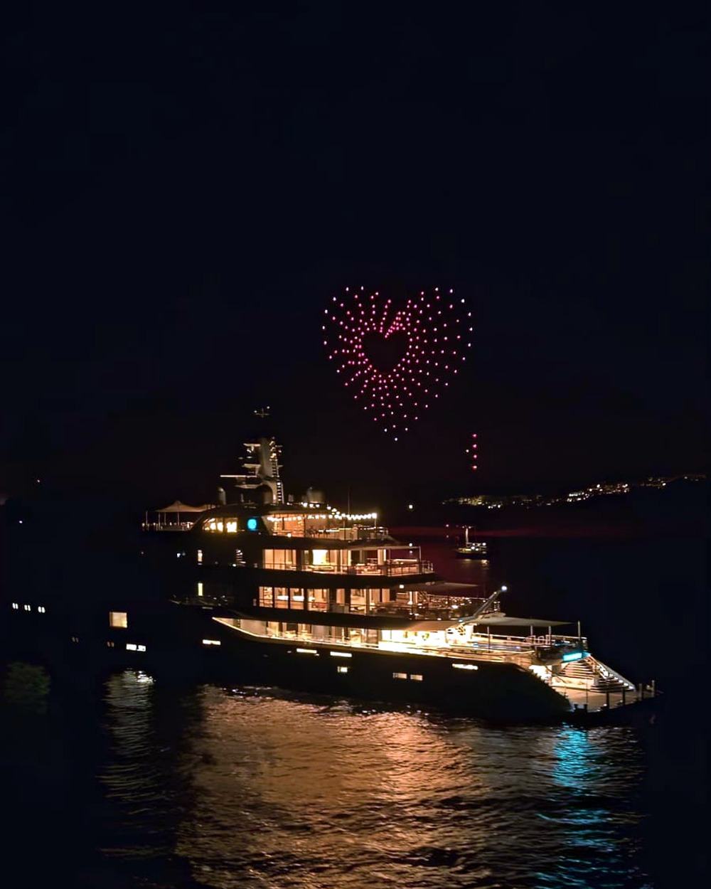 Red drone heart glowing above a luxury yacht at night