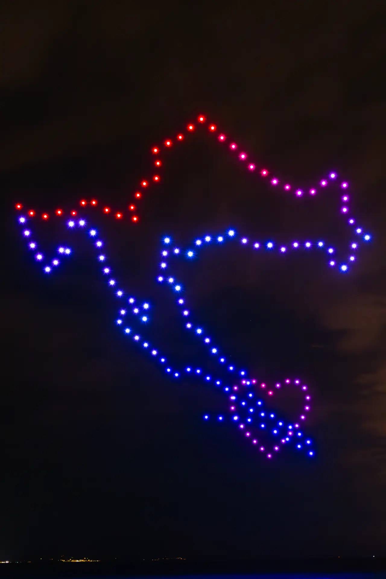 Drone formation of a heart and anchor glowing over the sea at night