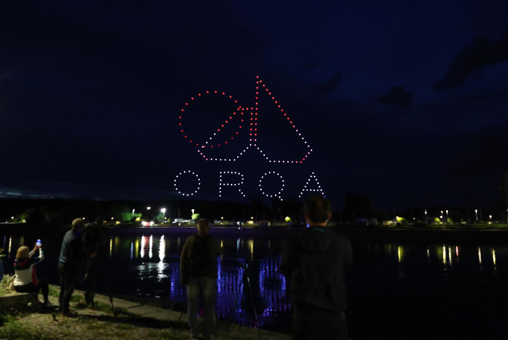 ORQA logo and text formation of drones above a waterfront crowd at night